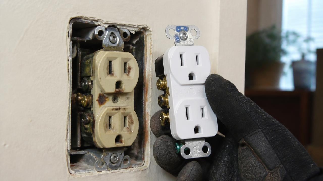 Worn, scorched beige wall outlet being replaced with a new white receptacle